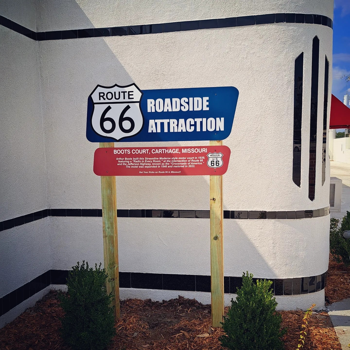 A sign that says "Route 66 Roadside Attraction. BOOTS COURT, CARTHAGE, MISSOURI. Arthur Boots built this Streamline Moderne style motor court in 1939, featuring a "Radio in Every Room, " at the intersection of Route 66 and the Jefferson Highway, known as the 'Crossroads of America'. The motel was expanded in 1946 and restored In 2022. Get Your Kicks on Route 66 in Missouri!"